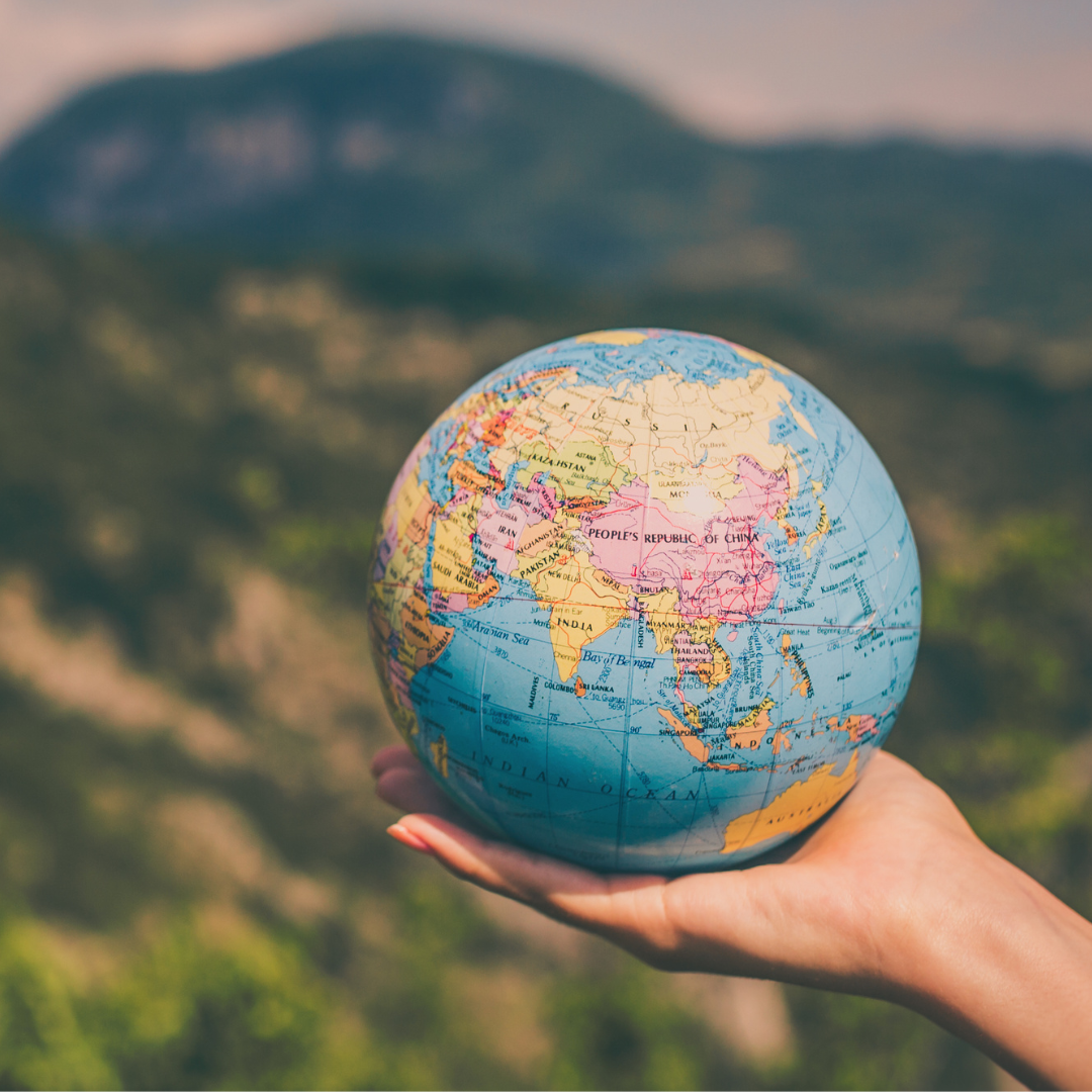 Hand hält Weltkugel, Berge im Hintergrund