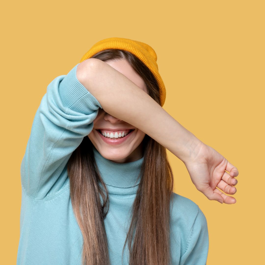 lächelnde Frau hält sich Hand vors Gesicht