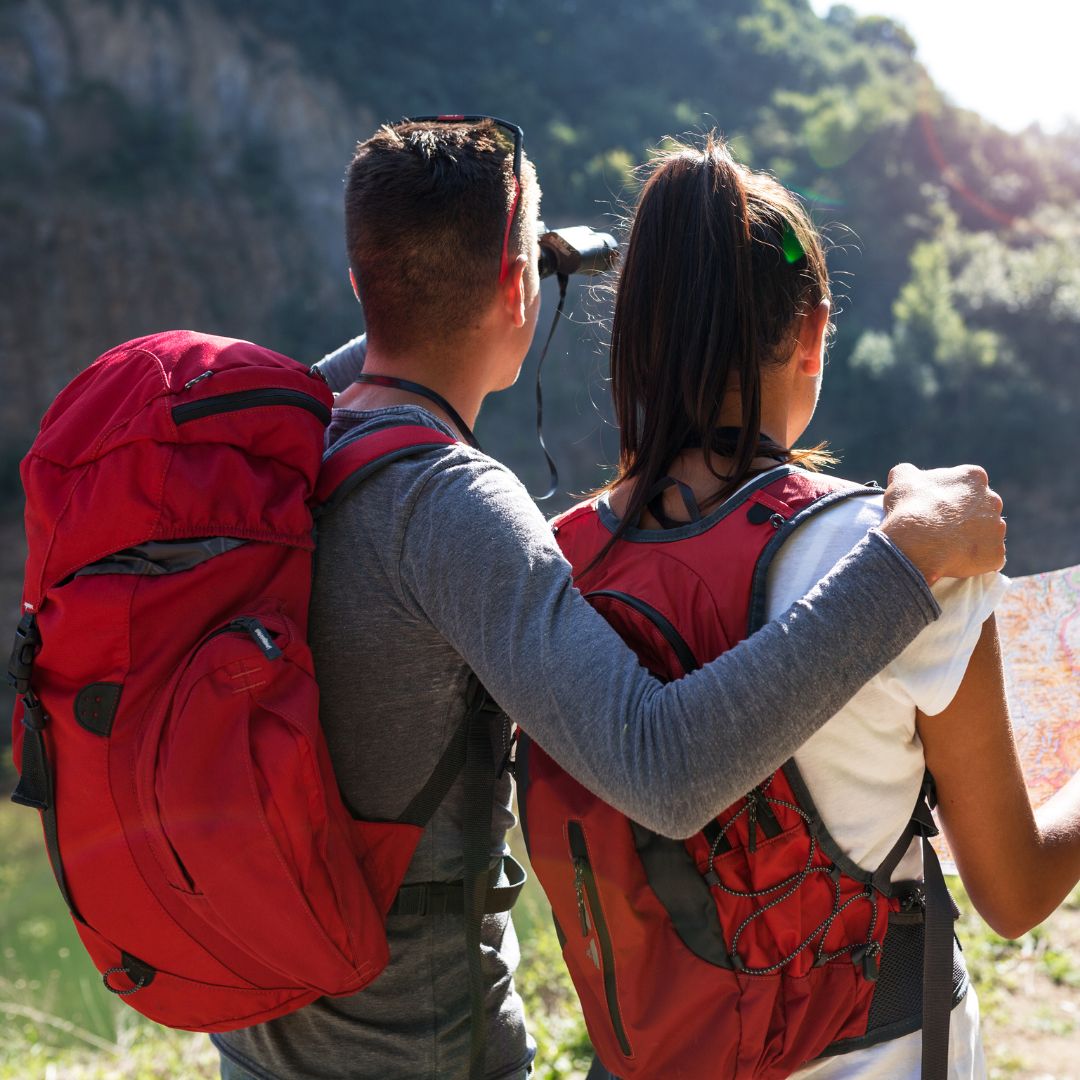 Mann und Frau mit Rucksäcken vor grüner Landschaft