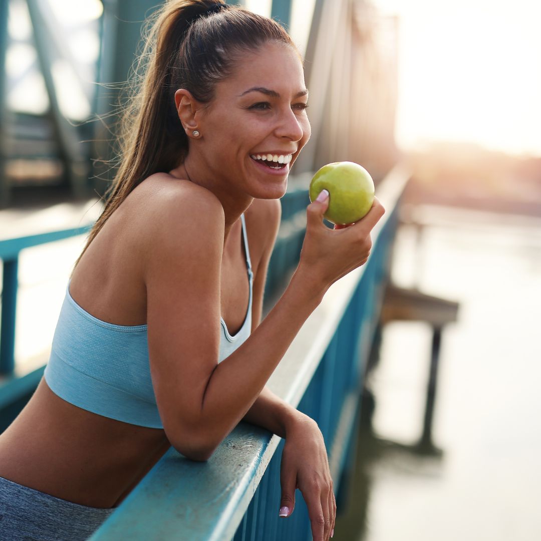 Frau in Sportkleidung schwitzt, lächelt und isst Apfel